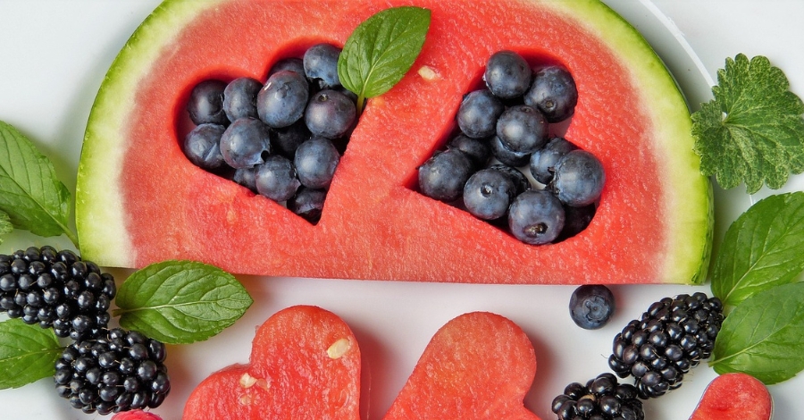Imagem com vista aérea de uma fatia de melancia com formato de coração e cheio de frutas parecidas com uvas